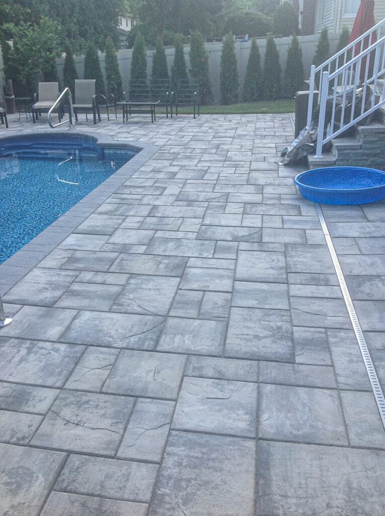 Grey concrete paver deck surrounding an in-ground pool with grey stone coping.