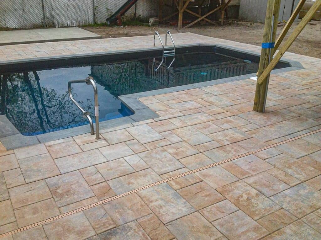 Grey and Tan mixed concrete paver deck surrounding an in-ground pool with grey coping.