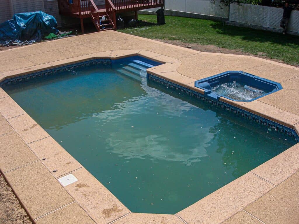Tan frontier desert deck surrounding an in-ground pool that includes coping and a spa.