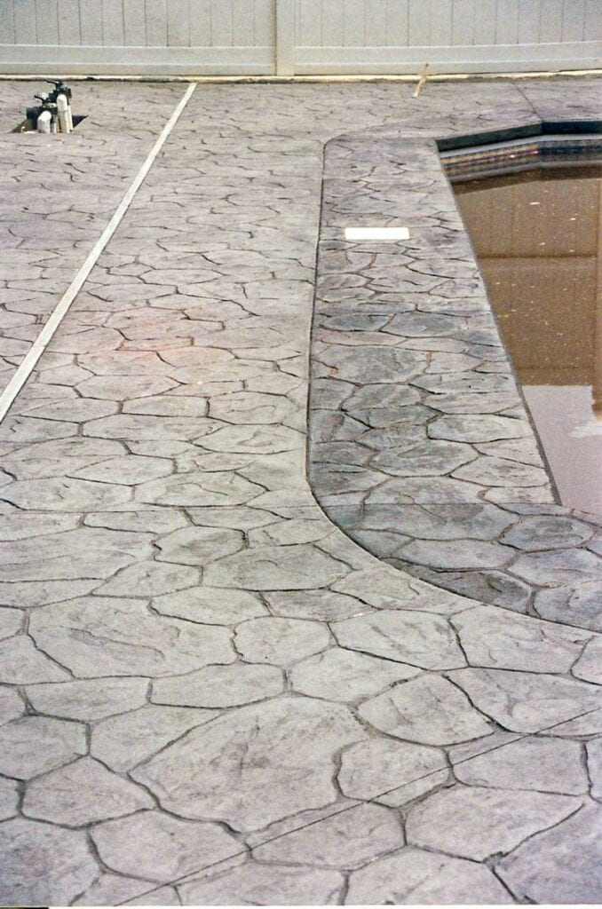 A grey stamped concrete deck surrounding a pool with slightly darker grey coping.
